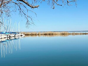 A calm lake with boats docked on the shore, clear skies, and sparse vegetation.