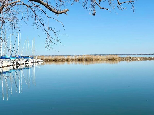 Een rustig meer met aan de oever afgemeerde boten, heldere lucht en schaarse begroeiing.