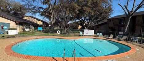 A swimming pool with a wooden deck, surrounded by a fence, and trees in the background.