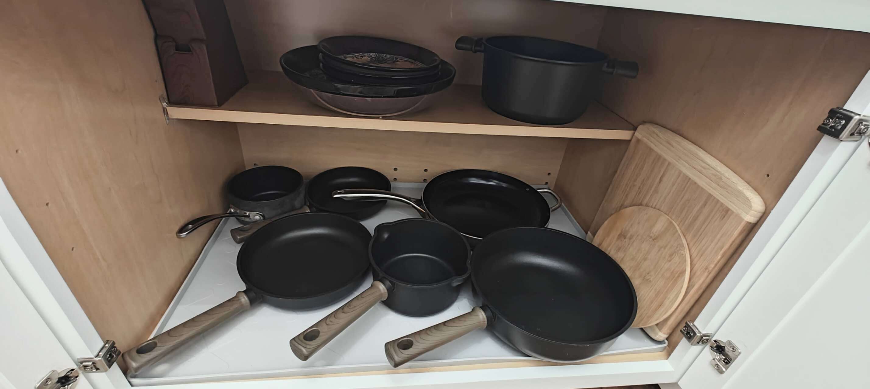 Un armari de cuina amb diverses paelles i cassoles negres, algunes amb nans de fusta.