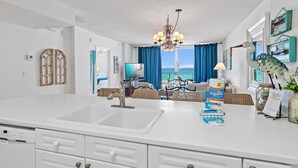 A modern kitchen with a large sink, white cabinetry, and a dining area with wicker furniture. - Island Princess 406 (Fort Walton Beach)