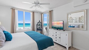 A bedroom with a bed, a television, a ceiling fan, a dresser, and a view of the ocean. - Island Princess 406 (Fort Walton Beach)