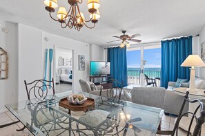 A modern living room with a glass dining table, comfortable seating, a ceiling fan, and a view of the ocean. - Island Princess 406 (Fort Walton Beach)