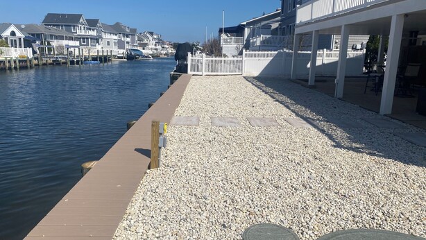Um calçadão à beira-mar com um píer de madeira, caminho de pedras e edifícios voltados para o mar.