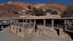A rustic building with stone walls, outdoor seating, and a mountain backdrop. - Hosteria Terrazas de la Posta (Purmamarca)