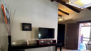 A bedroom with a bed, a TV on a wooden stand, a framed picture on the wall, and a door leading to an outdoor area. - Hosteria Terrazas de la Posta (Purmamarca)