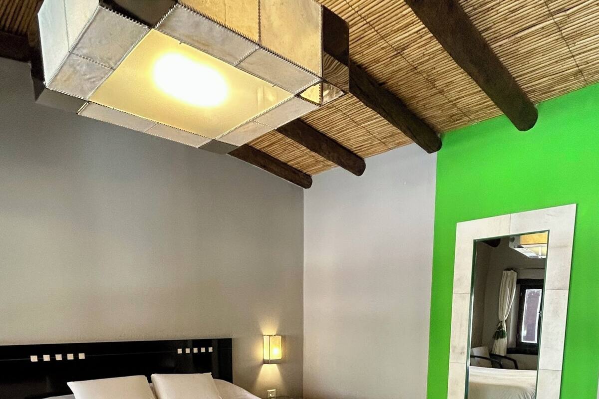Une chambre à coucher avec un lit, une lampe de chevet, un banc et un miroir au mur.