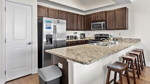 A kitchen with granite countertops, stainless steel appliances, wooden cabinets, and a white door. - Alerio D301 (Miramar Beach)