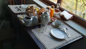 Een ontbijttafel gedekt met thee, koffie, brood en fruit, met uitzicht op bomen.