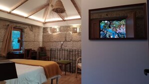 Een kamer met een bed, een bureau, een stoel, een televisietoestel en stenen muren.
