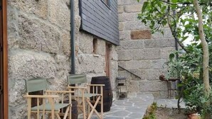 Un edificio de piedra con techo oscuro, mesas al aire libre y un pequeño jardín.