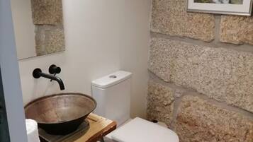 A bathroom with a stone wall, a wooden sink, a white toilet, and a framed picture on the wall.