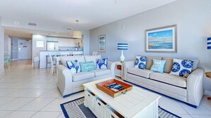 A modern living room with a sofa, coffee table, and a dining area in the background. - Sterling Shores 408 (Destin)
