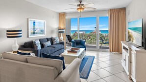 A living room with a sofa, armchair, coffee table, TV, and a view of the ocean. - Sterling Shores 408 (Destin)