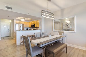 Une cuisine moderne dotée d’appareils électroménagers en acier inoxydable, un coin repas avec une longue table et des chaises, et un grand miroir au-dessus du comptoir.