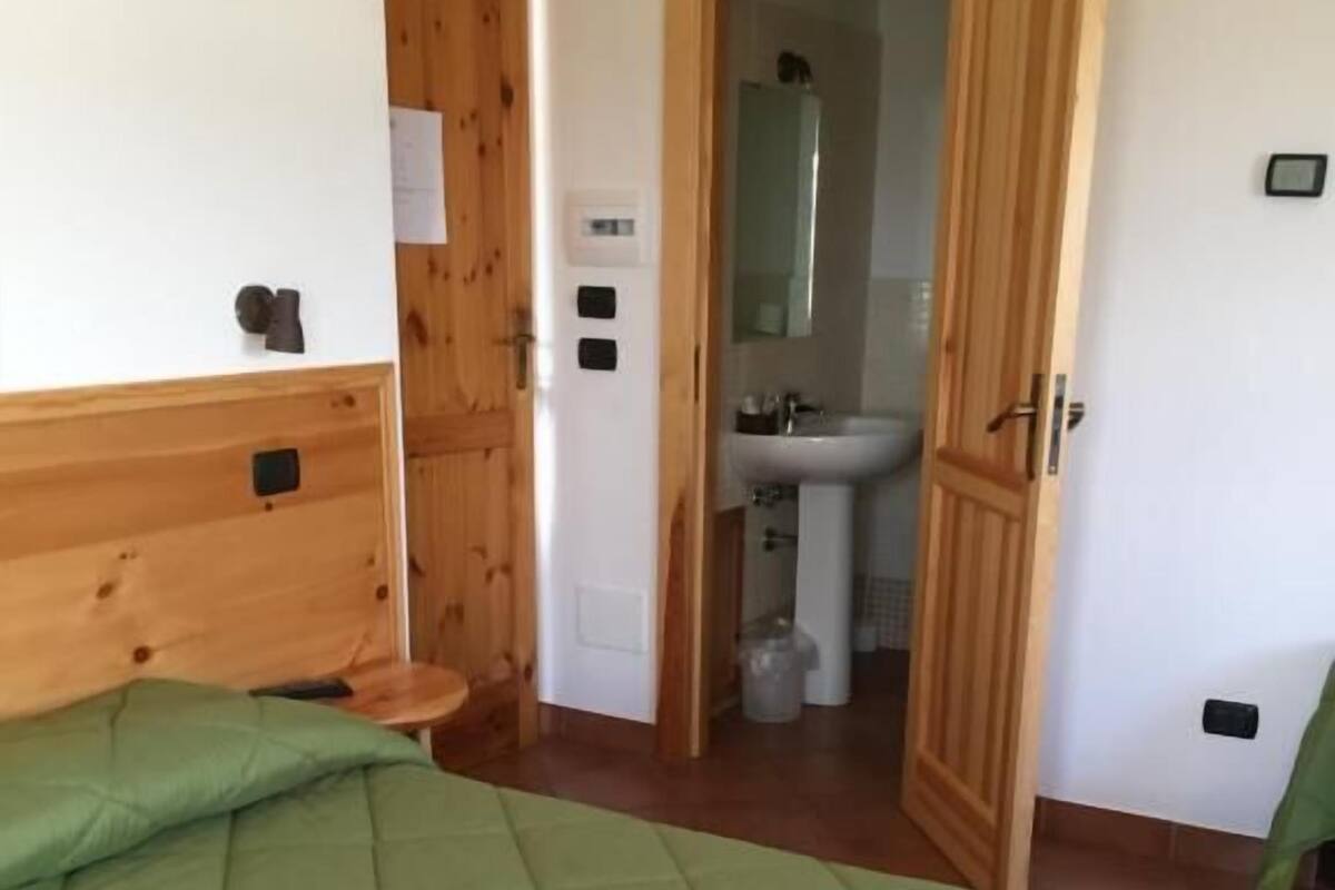 Une pièce avec un lit, une porte en bois, une salle de bain avec un lavabo et un miroir.
