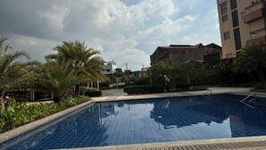 A swimming pool with tiled flooring, surrounded by greenery and buildings.