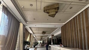A hotel lobby with a long reception desk, a patterned ceiling, and a tiled floor.