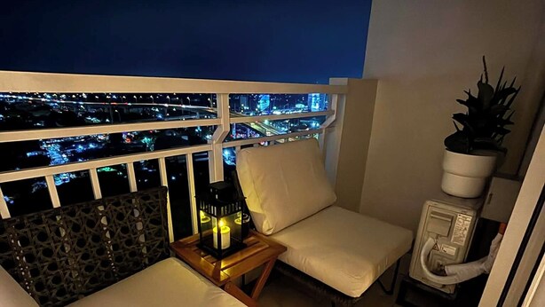 A balcony with two chairs, a small table with a lantern, and a potted plant.