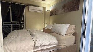 A bedroom with a bed, a window with curtains, an air conditioning unit, and a wall-mounted artwork.