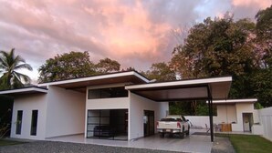 A modern house with a covered driveway, a garage, and a gravel front yard. - Stylish 3BR Villa w/ Pool at Marino Ballena (Uvita)