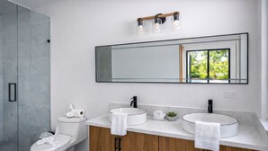 A modern bathroom with a glass shower enclosure, a toilet, a vanity with two sinks, and a large mirror. - Stylish 3BR Villa w/ Pool at Marino Ballena (Uvita)
