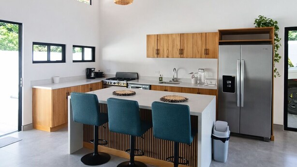 A modern kitchen with a central island, wooden ceiling, pendant lights, and a stainless steel refrigerator. - Stylish 3BR Villa w/ Pool at Marino Ballena (Uvita)