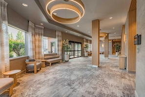 A spacious lobby with a modern design, featuring a seating area with sofas and chairs, a large window offering a view of the outdoors, and a unique circular ceiling light fixture. - The Mindaro, part of JdV by Hyatt (Portland)