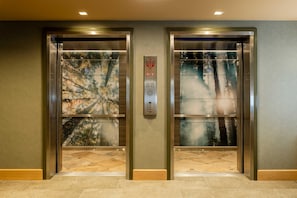 Two elevator doors with a forest view, a control panel with emergency instructions, and a textured wall. - The Mindaro, part of JdV by Hyatt (Portland)