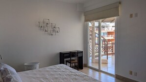 Ein Schlafzimmer mit Bett, Schreibtisch, Stuhl, Deckenventilator und einer Schiebetür zu einem Außenbereich.