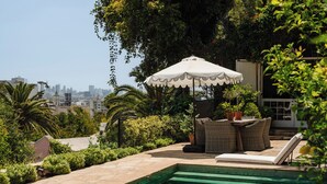 A poolside area with a view of a city skyline, a white umbrella, wicker furniture, and a stone pathway. - Private Hollywood Hills View Estate 4BR (Los Angeles)