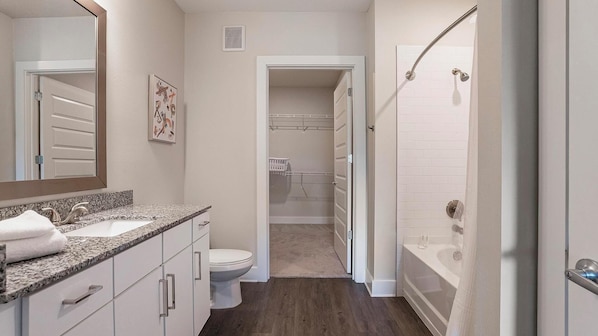 A modern bathroom with a granite countertop, a toilet, a walk-in shower, and a walk-in closet. - Landing Furnished Apartments near FSU (Tallahassee)