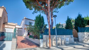 Une rue résidentielle bordée de maisons, avec un arbre, un lampadaire et une entrée fermée par un portail.