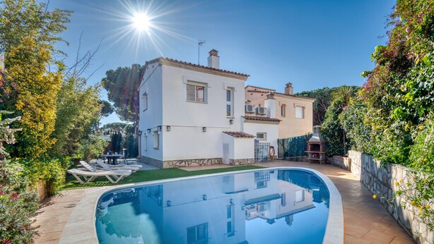 Une maison à deux étages avec une piscine, entourée de verdure et sous un ciel dégagé.