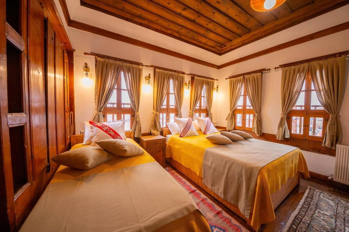 Une chambre avec deux lits, des poutres en bois et de grandes fenêtres avec des rideaux.