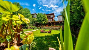 Un jardin avec une pelouse, un banc en bois et un bâtiment doté d’un balcon.