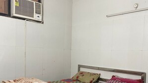 A single bed with a patterned bedspread, pillows, and a blanket. There is a wall-mounted air conditioning unit and a light switch on the wall. - Usethis space to grab a guest'stoattractions or suitability(like family-friendly (Vrindavan)