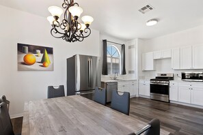 Una cocina moderna con armarios blancos, electrodomésticos de acero inoxidable y un comedor con mesa y sillas de madera.