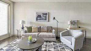 A living room with a sofa, armchair, coffee table, floor lamp, and artwork on the wall.