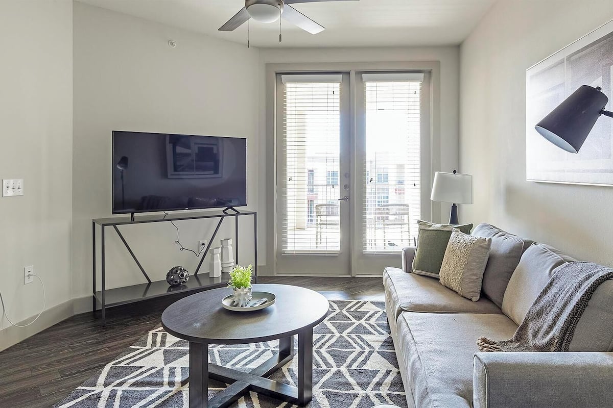 A living room with a sofa, a coffee table, a TV on a stand, and a ceiling fan.