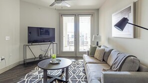 Un salon comprenant un canapé, une table basse, un téléviseur posé sur un meuble et un ventilateur de plafond.