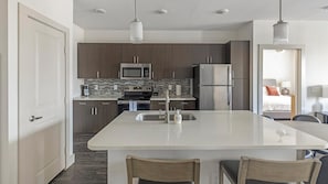 A modern kitchen with dark wood cabinets, stainless steel appliances, and a central island with a sink. - Landing Apartments Midtown Park (Dallas)