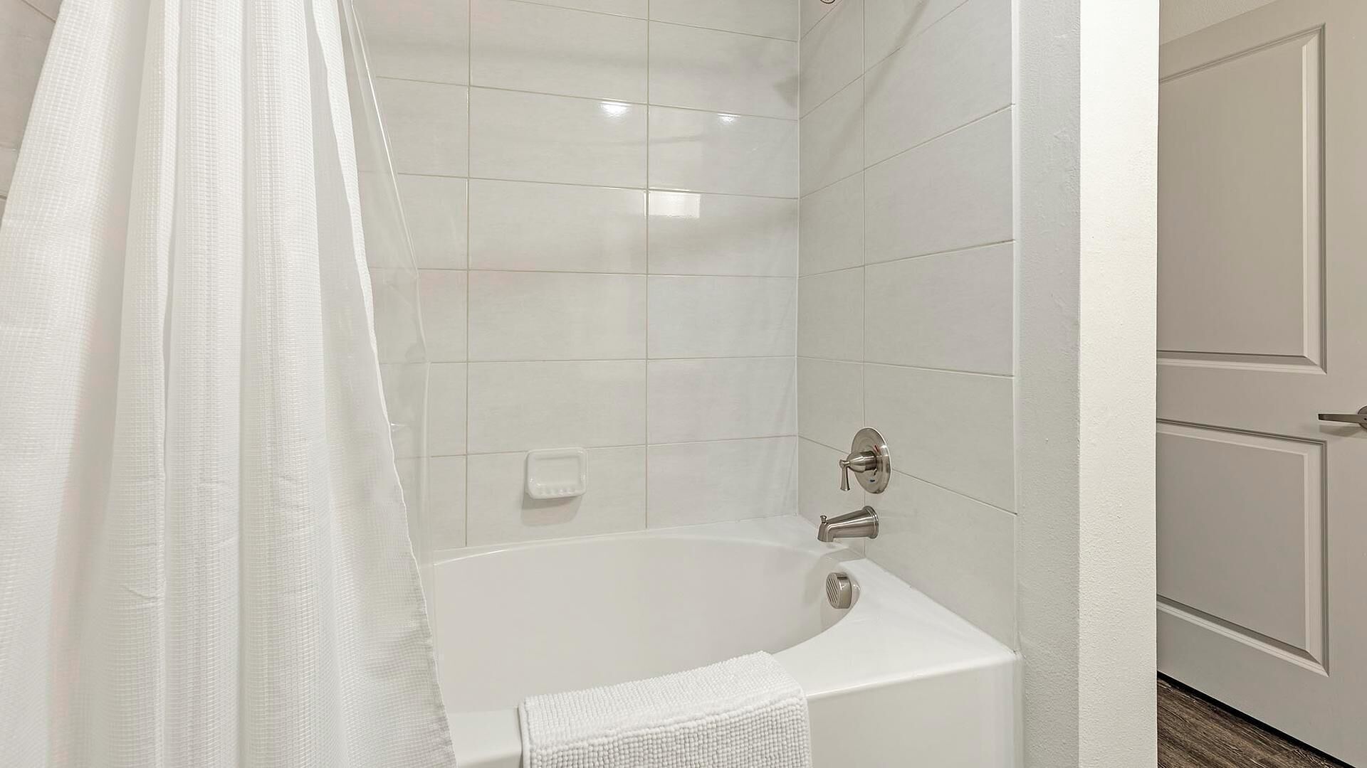 A bathroom with a bathtub, a shower curtain, and tiled walls.