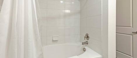 A bathroom with a bathtub, a shower curtain, and tiled walls.