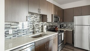 A modern kitchen with dark wood cabinets, a stainless steel refrigerator, a microwave, and a tiled backsplash. - Landing Apartments Midtown Park (Dallas)