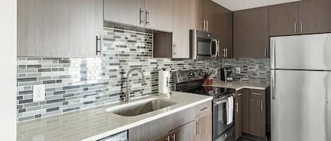 A modern kitchen with dark wood cabinets, a stainless steel refrigerator, a microwave, and a tiled backsplash.