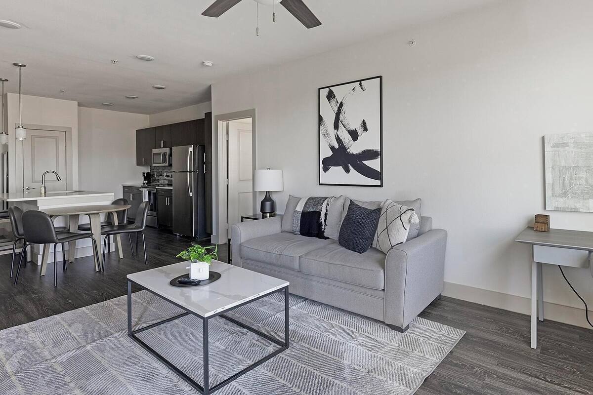 A modern living room with a grey sofa, a coffee table, and a dining area with chairs.