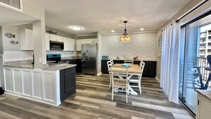 A modern kitchen with a central island, a dining area with a table and chairs, and a view of a building through a large window. - Ocean View-Family Friendly condo, 211B, in Myrtle Beach Resort (Myrtle Beach)