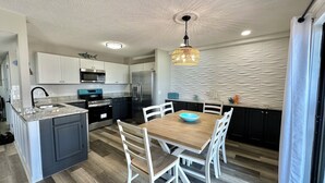 A modern kitchen with a central island, white cabinetry, stainless steel appliances, and a dining area with a wooden table and white chairs. - Ocean View-Family Friendly condo, 211B, in Myrtle Beach Resort (Myrtle Beach)