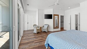 Un dormitorio con una cama grande, un ventilador de techo, un televisor y sillas de mimbre.